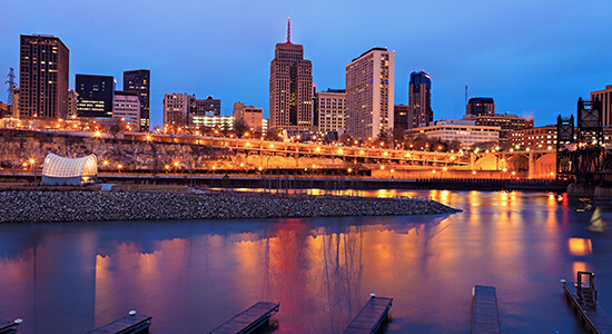 A city skyline with buildings lit up at night.