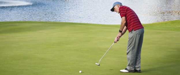 Golfer putting on green near water hazard.