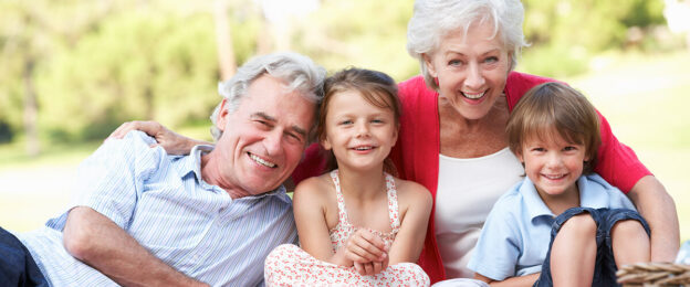Grandparents and grandchildren smiling outdoors together.