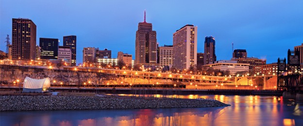 Lit downtown skyline at dusk with river reflections